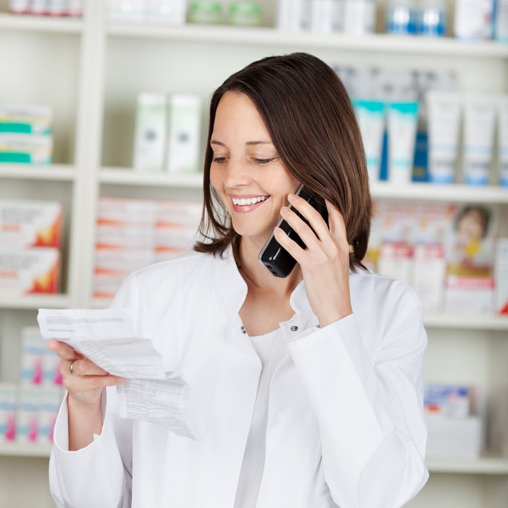 Mid adult female pharmacist holding prescription paper while using cordless phone in pharmacy